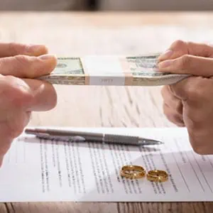 Two individuals holding cash over a document with a pen and wedding rings