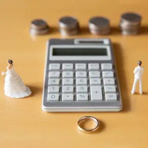 Tiny bride and groom on calculator with wedding ring, symbolizing marriage and finance.