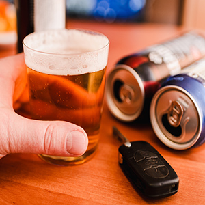 Hand holding a beer with car keys and cans, illustrating a DUI and Ignition Interlock Devices in Washington