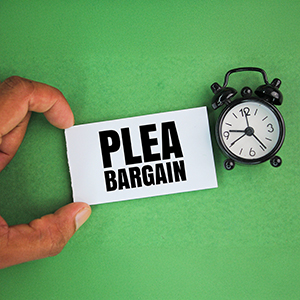Hand holding a PLEA BARGAIN card next to an alarm clock, relating to a misdemeanor case in Washington